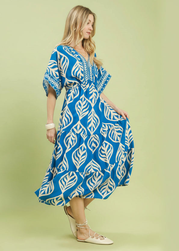 Woman wearing a blue and white patterned dress on a light green background with Umgee branding.
