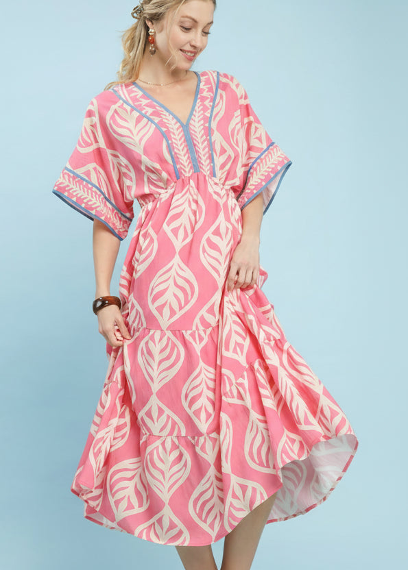 Woman wearing a pink dress with white leaf pattern on a light blue background, featuring Umgee Exclusive branding.