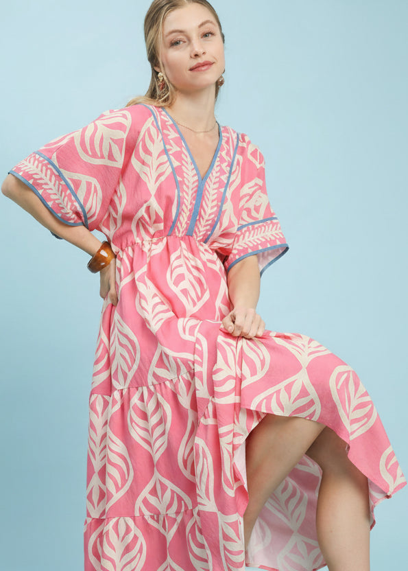 Woman wearing a pink and white patterned dress on a light blue background with Umgee branding.