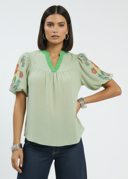 Woman wearing a green blouse with floral embroidery on sleeves against a white background
