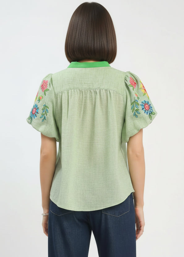Green blouse with floral embroidery on sleeves worn by a person, against a white background.