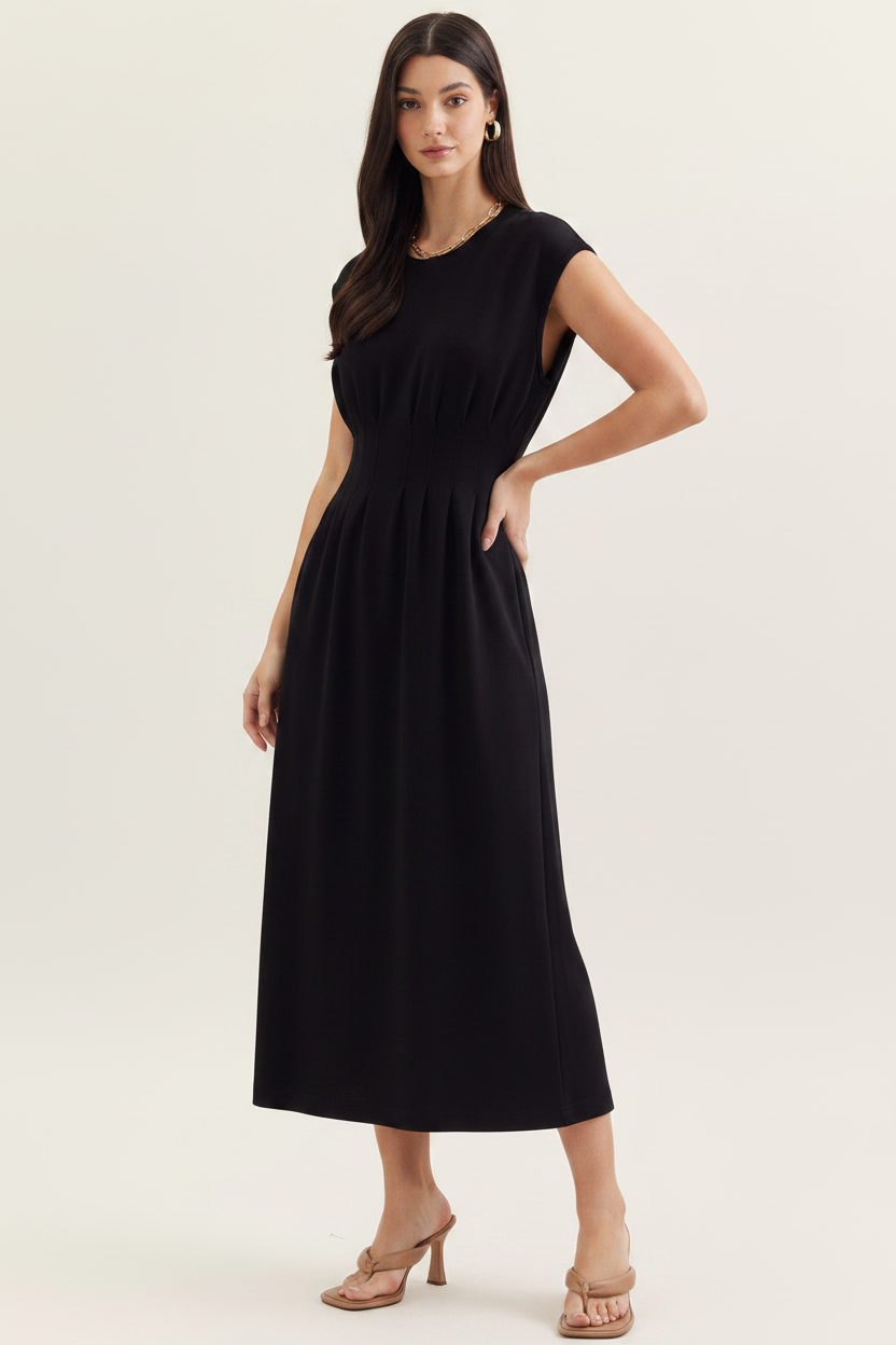 A woman modeling a sleeveless black midi dress with a gathered waist and straight skirt, paired with beige strappy heels, against a plain light beige studio background.