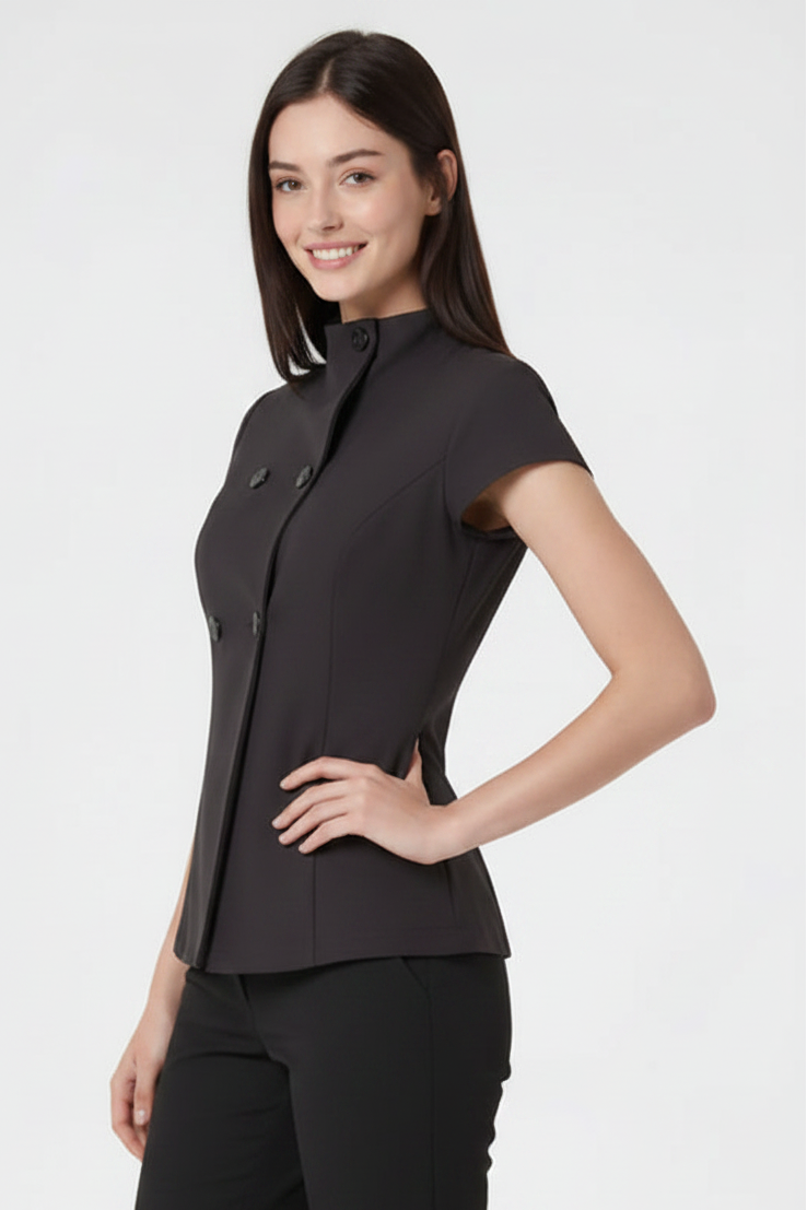 A woman modeling a black short-sleeve double-breasted blazer with a high stand-up collar and structured shoulders, paired with black trousers, against a plain light gray studio background.