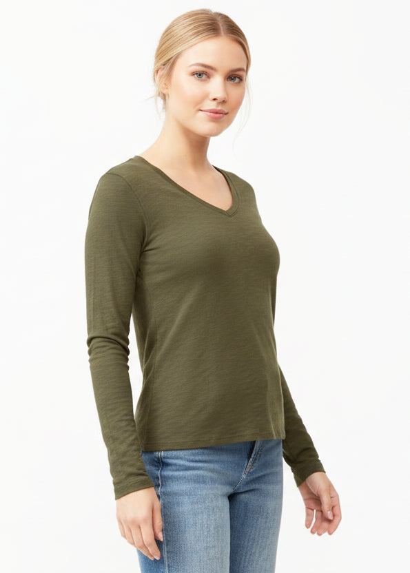 Woman wearing an olive green long-sleeve top and blue jeans on a white background