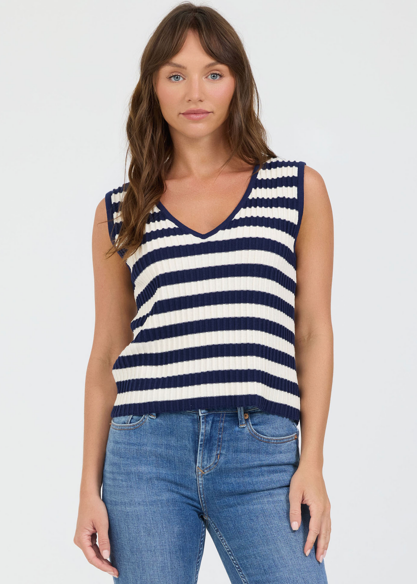 Woman wearing a navy and white striped sleeveless top with blue jeans on a white background