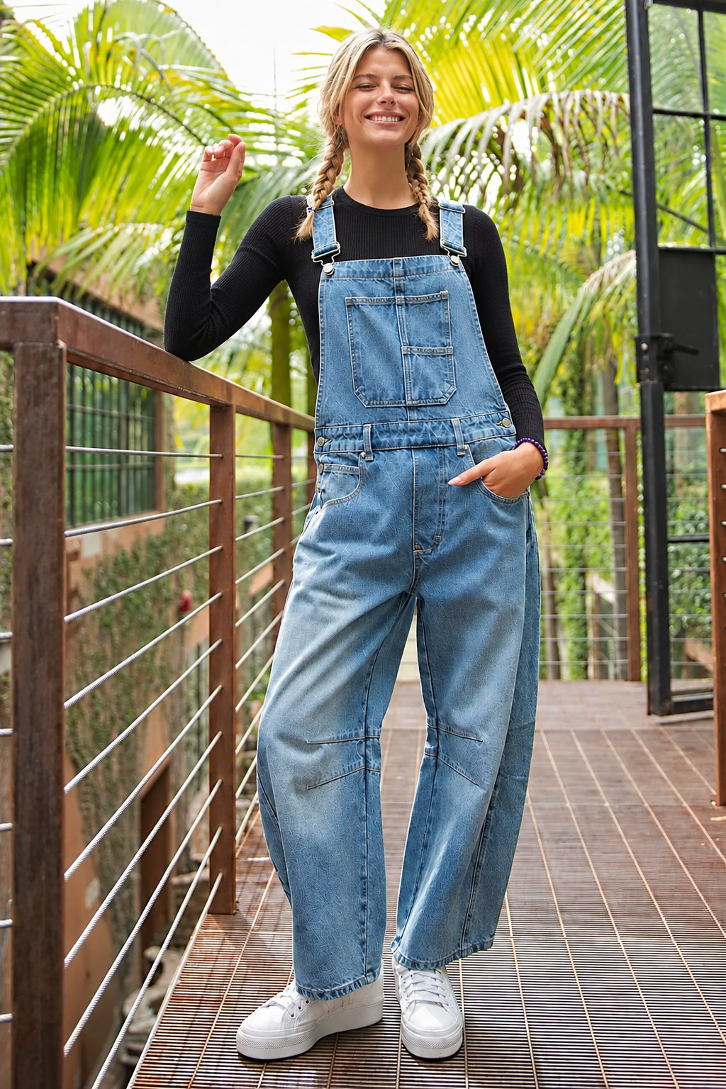 Mineral washed sleeveless denim jumpsuit featuring a square neckline, adjustable straps, a front bib design with a 3 pocket opening, belt loops, buttons on the side for added comfort, two side hip pockets, two back pockets, added seams in the back, is a barrel leg design and is a relaxed fit body.