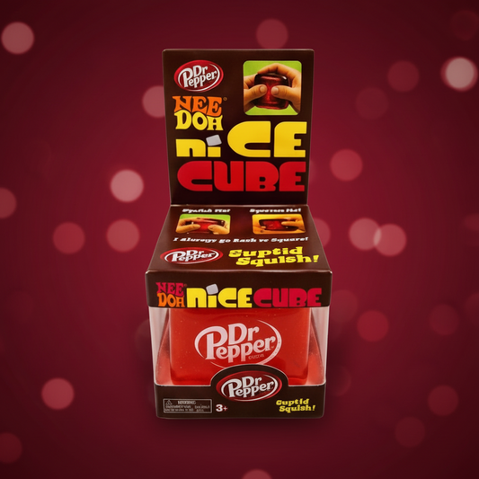 Dr Pepper Nee Doh Nice Cube Supid Squishy toy in its retail packaging, featuring a red cube with Dr Pepper branding on a dark brown display stand against a maroon bokeh background.