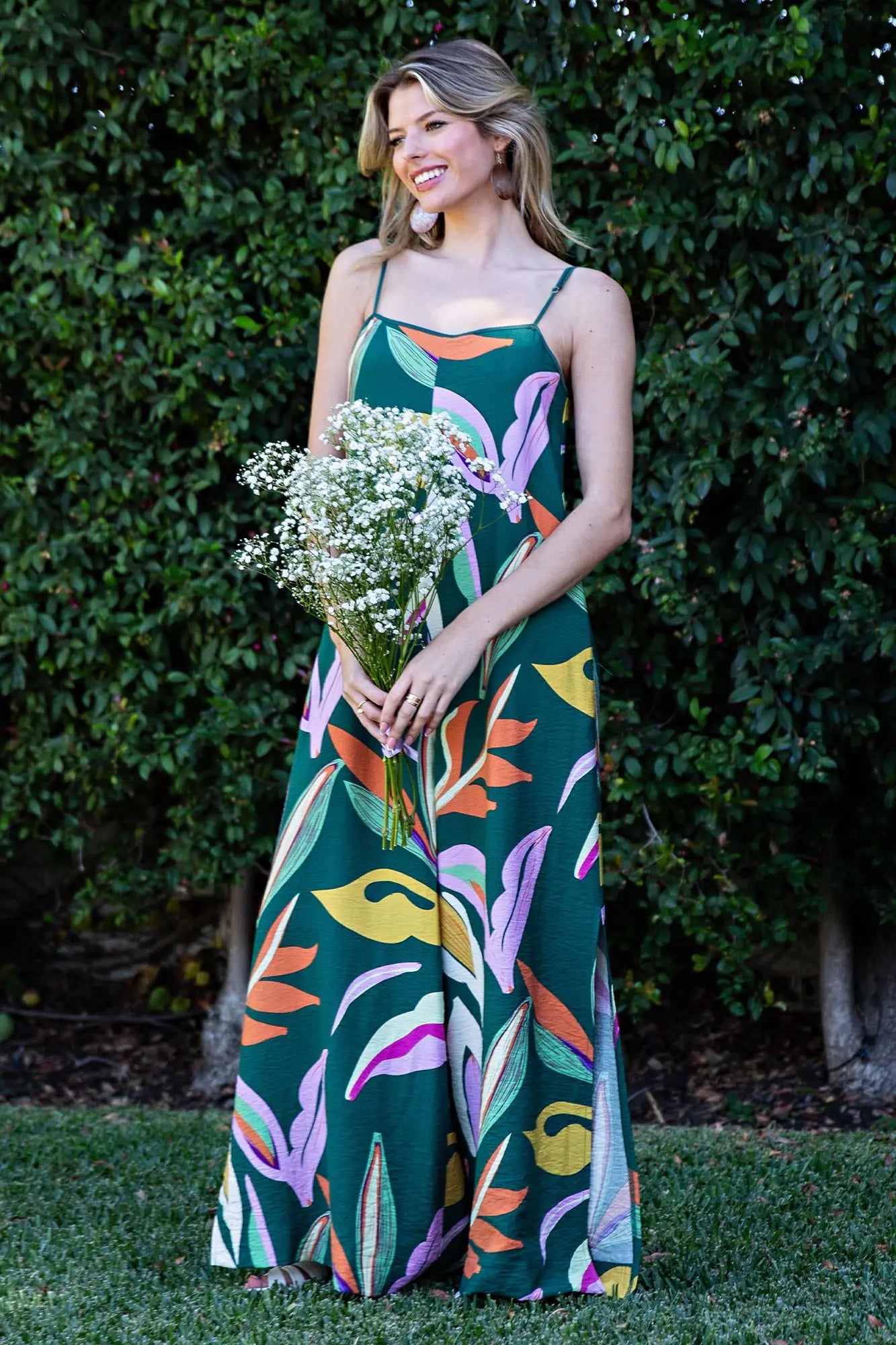 Woman in a colorful dress holding flowers against a green leafy background