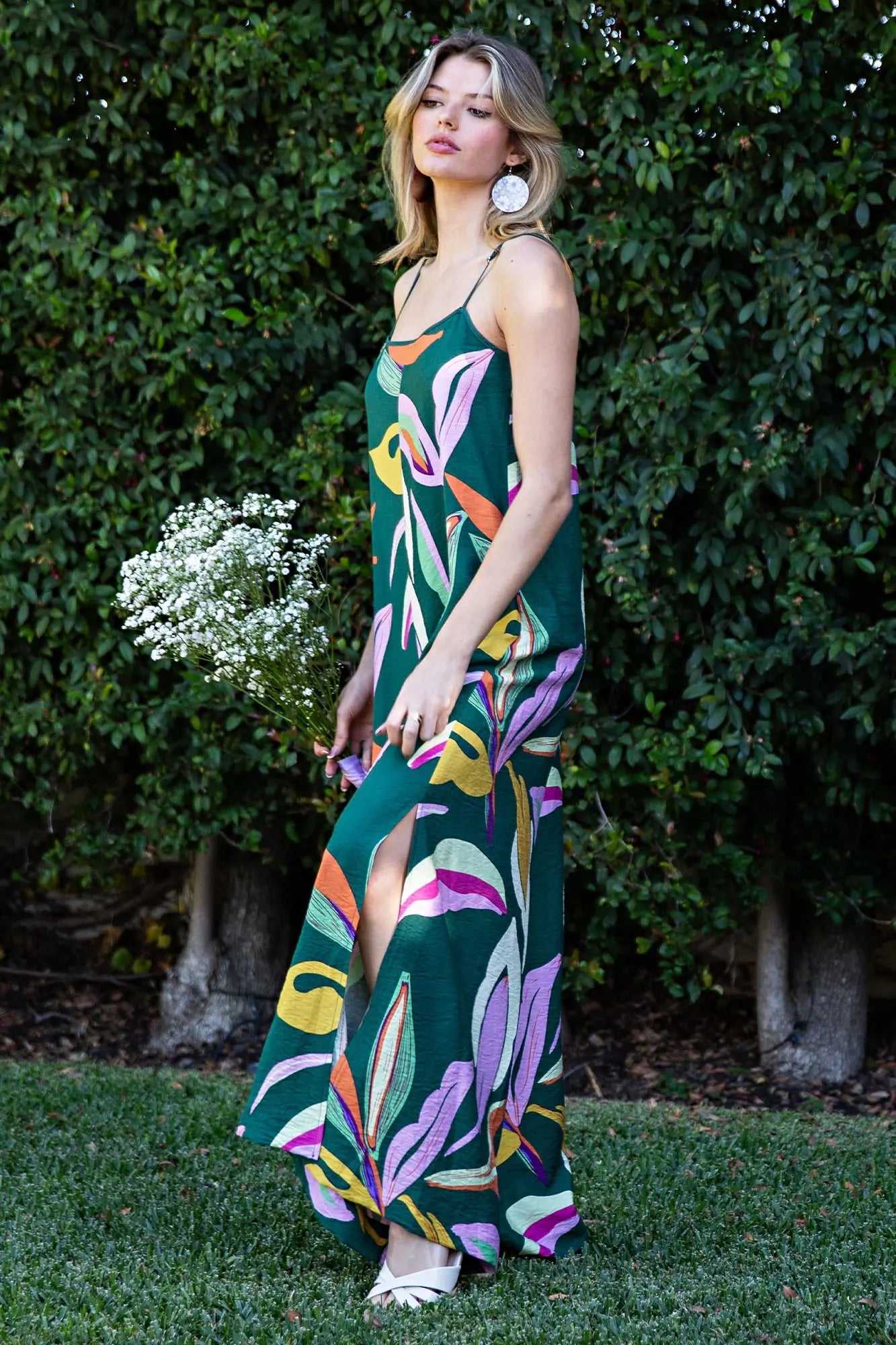 Woman wearing a colorful floral dress standing in front of greenery