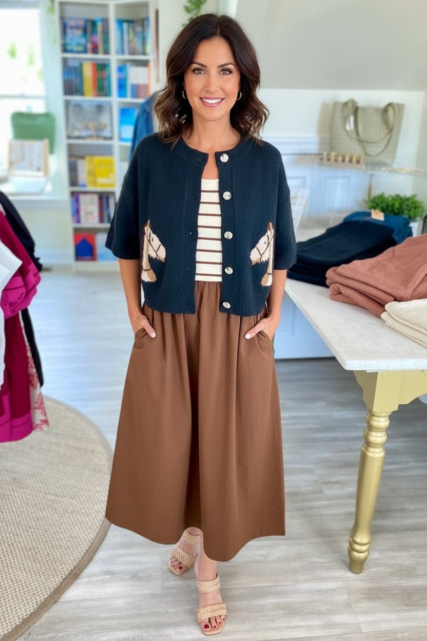 Woman in a stylish outfit standing in a room with books and a table.