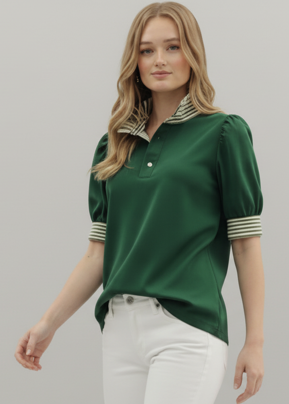 Woman wearing a green polo shirt with striped cuffs on a plain background