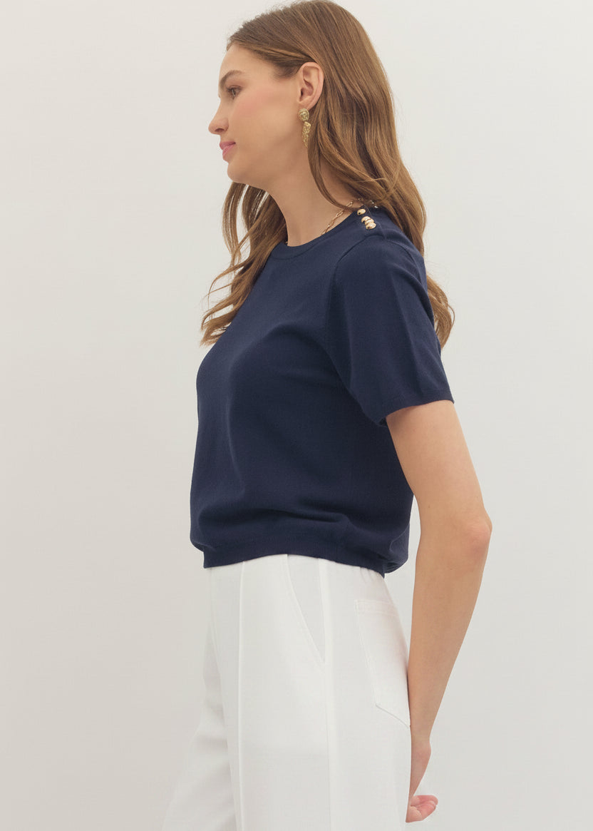 Woman wearing a navy blue top and dark pants on a light background