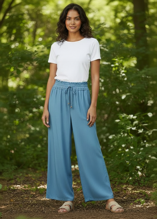 Woman wearing a white t-shirt and blue wide-leg pants standing in a forest.