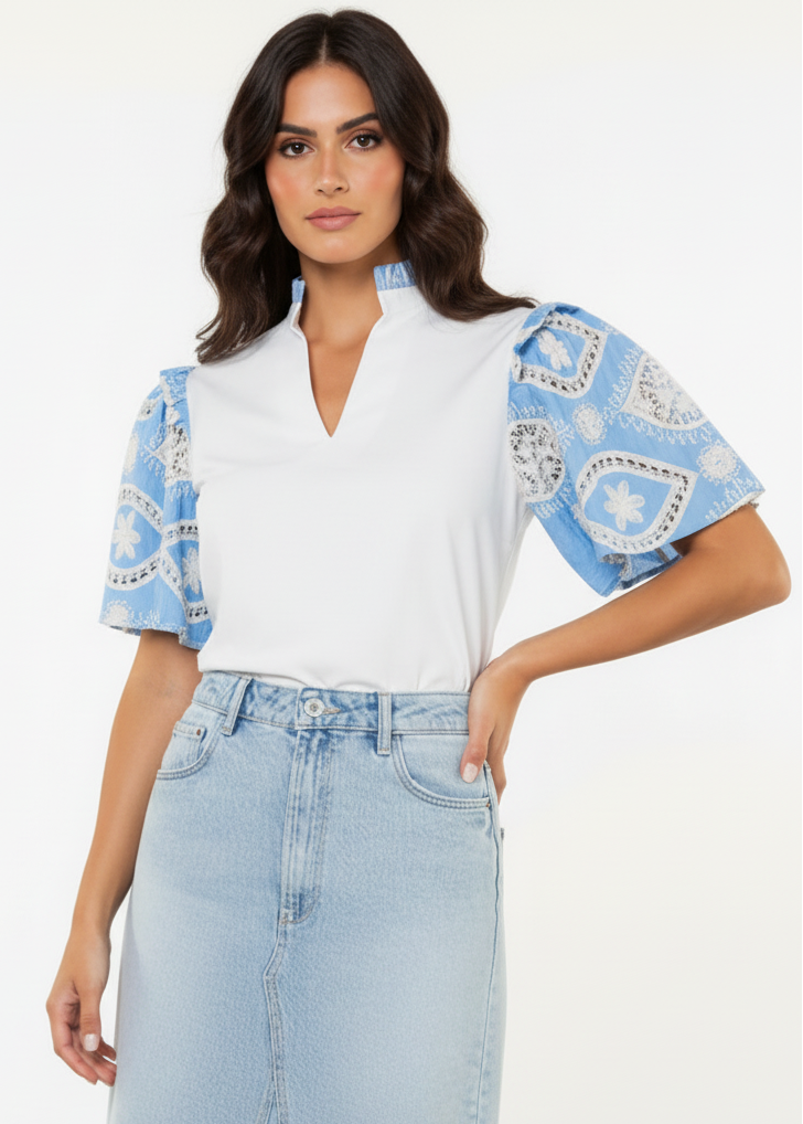 Woman wearing a white blouse with blue patterned sleeves and light blue jeans on a white background