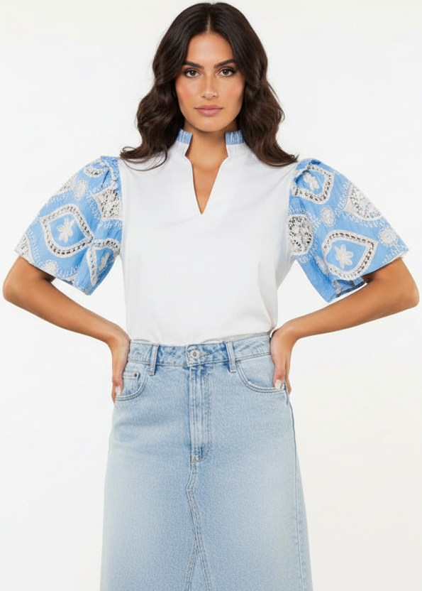 Woman wearing a white top with blue patterned sleeves and light blue jeans on a white background
