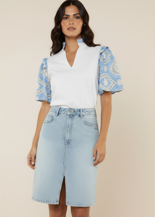 Woman wearing a white blouse with blue patterned sleeves and a light blue denim skirt on a beige background
