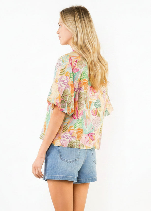 Woman wearing a colorful floral kimono-style top with beige shorts on a white background
