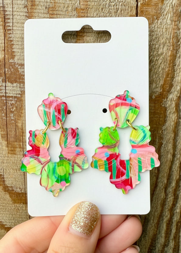 Colorful earrings on a branded card held by a hand against a wooden background