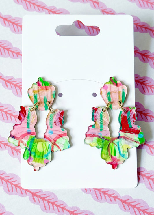 Colorful earrings on a Sandy Rizzo branded card with a pink and white feather pattern background.