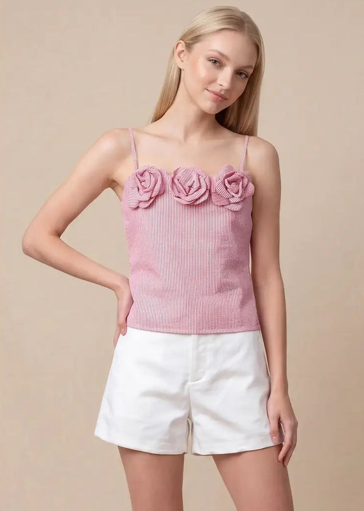 Woman wearing a pink top with floral details and white shorts on a beige background