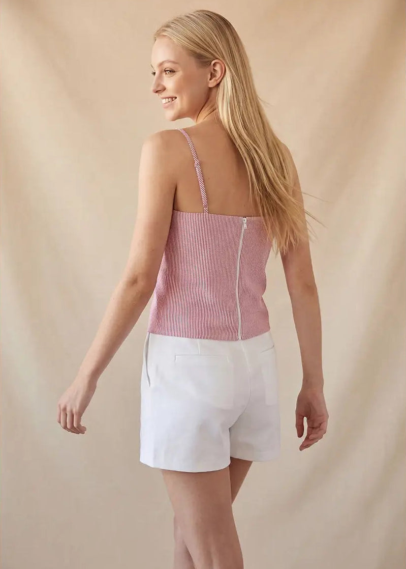 Woman wearing a pink top and white shorts against a beige background