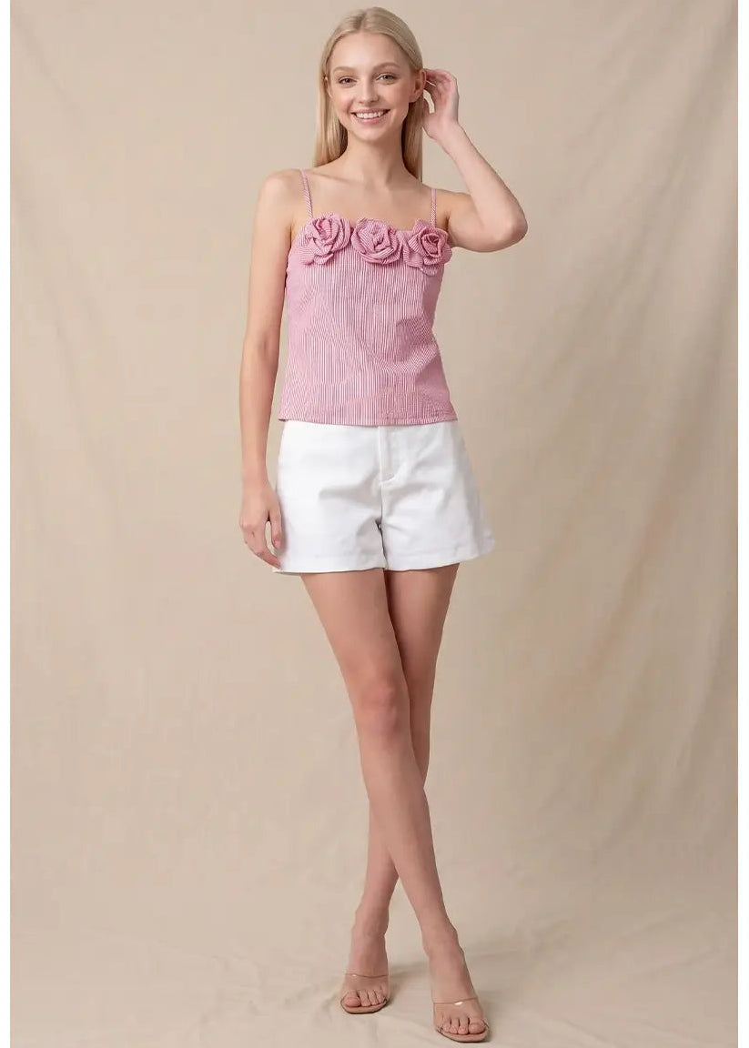 Woman wearing a pink top with floral details and white shorts on a beige background