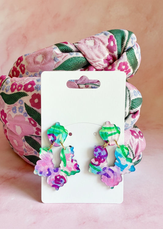 Colorful earrings on a display card with a floral scrunchie in the background.