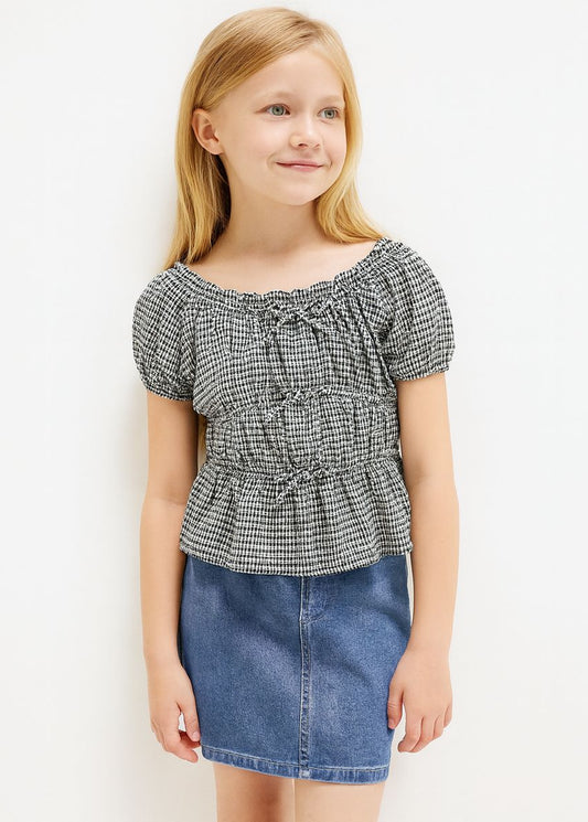 Young girl wearing a checkered top and denim skirt on a white background