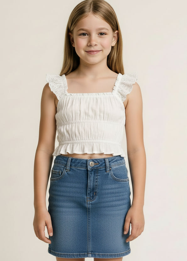 Young girl wearing a white dress with ruffled straps against a plain background