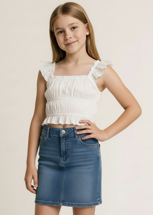 Young girl wearing a white top with ruffled sleeves and a blue denim skirt on a beige background