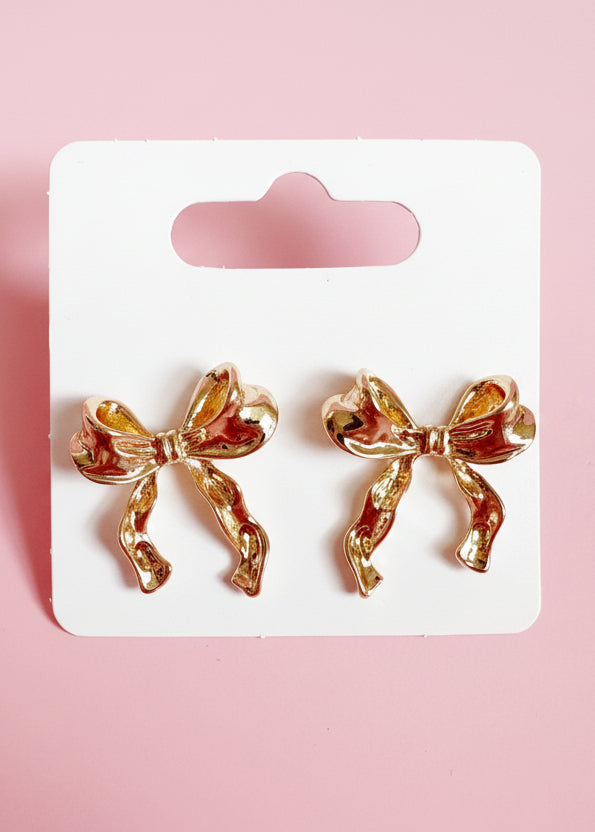 Bow-shaped earrings on a white card with pink background