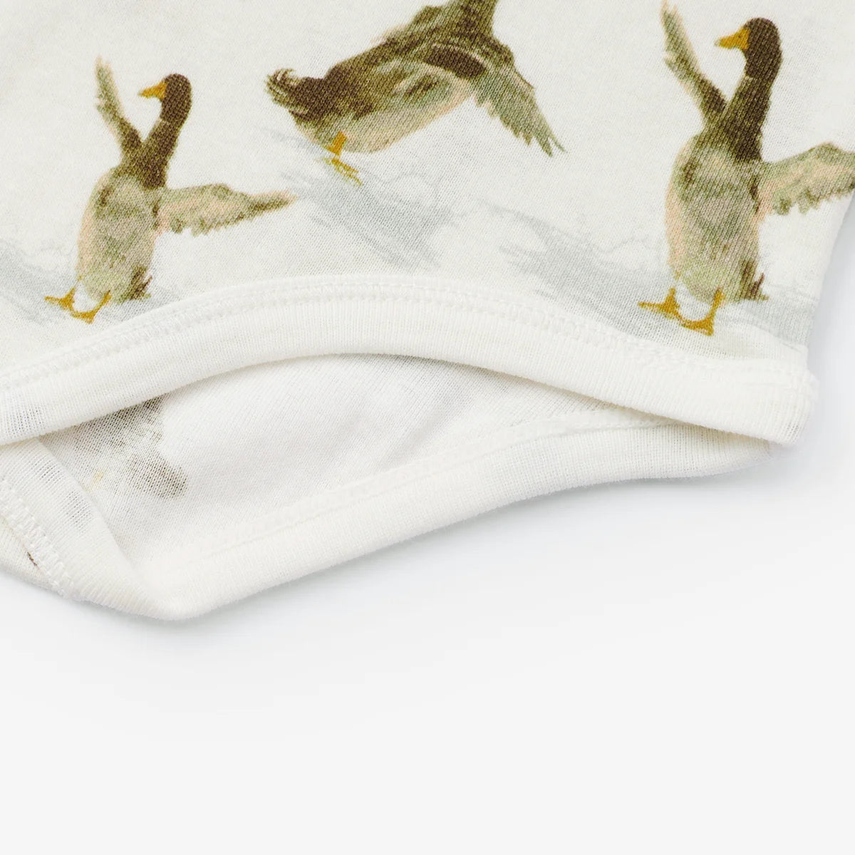 Close-up of a white fabric item, likely a baby blanket or soft textile, featuring a printed pattern of mallards in flight and standing, with a folded hem.