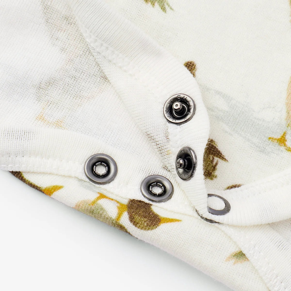 Close-up of a white baby garment or fabric panel with a subtle leaf print and dark metal snap buttons along the edge.