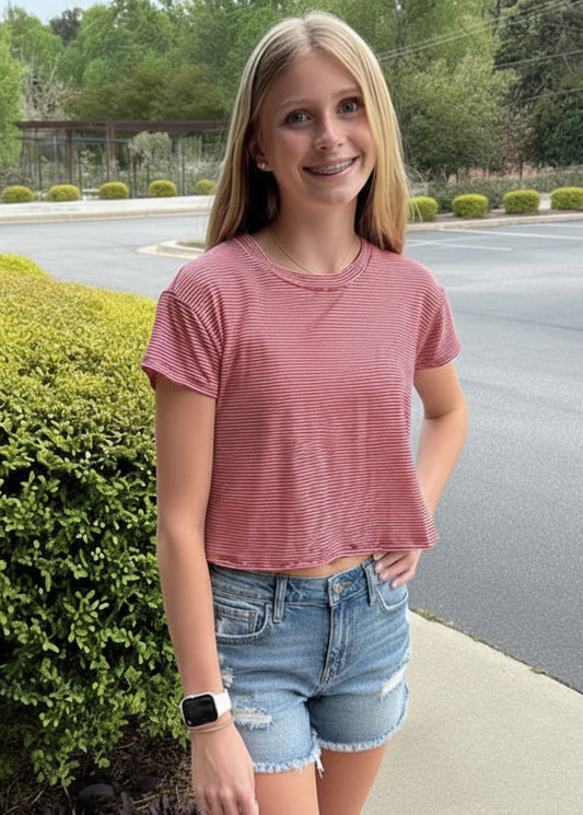 Woman in pink shirt and denim shorts standing on a sidewalk with a parking lot in the background