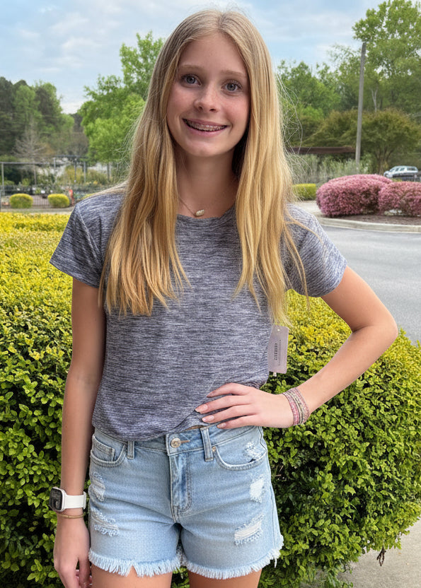 Woman in a gray t-shirt and denim shorts standing outdoors on a sidewalk.