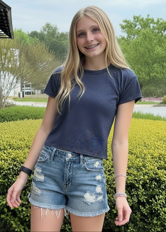 Person wearing a blue shirt and denim shorts standing outdoors with greenery in the background