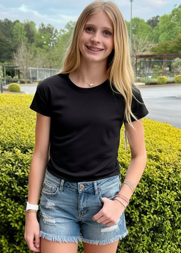 girl wearing a black t-shirt and denim shorts standing outdoors near a building.