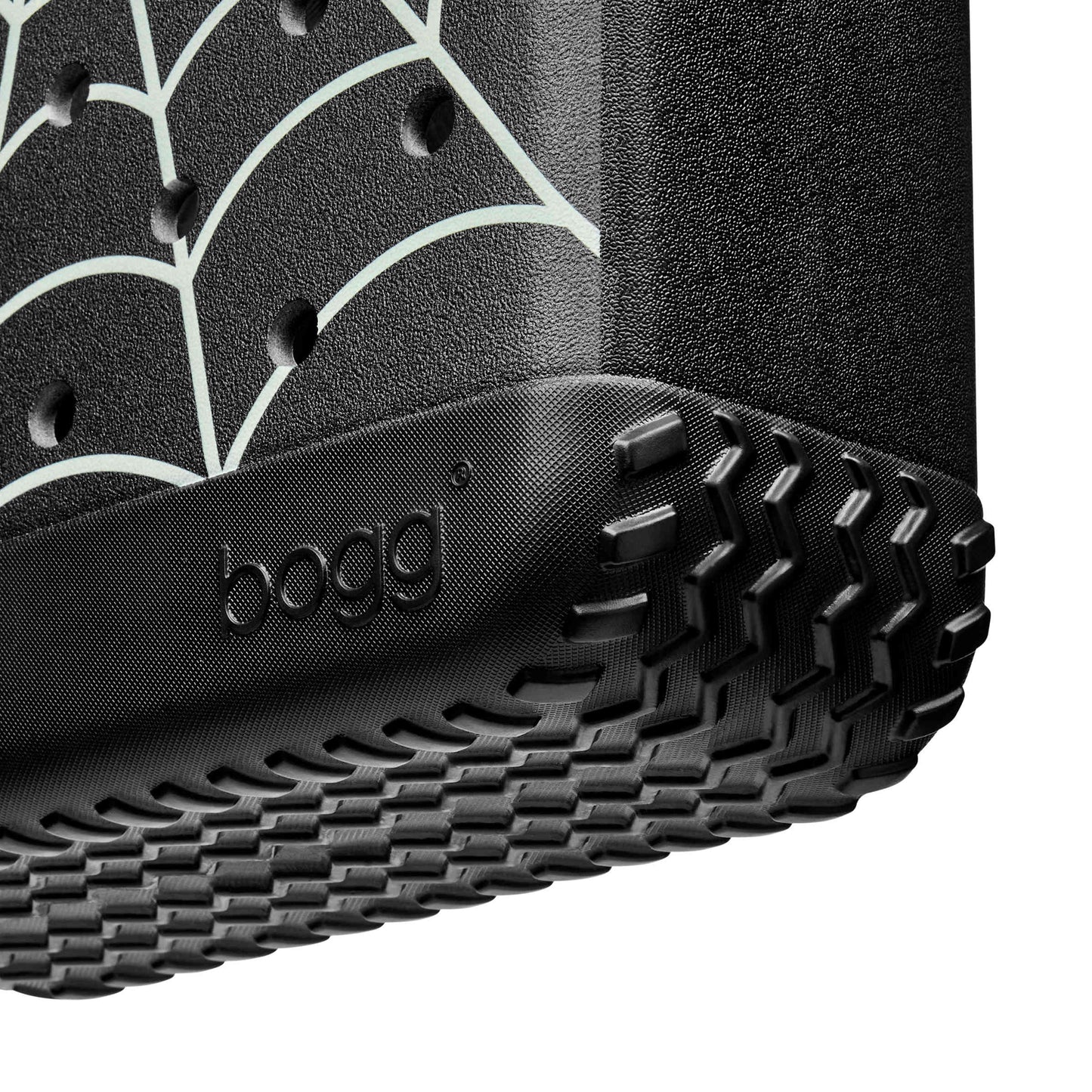 Close-up of a black Bogg Bag with a rugged treaded bottom edge and a white spiderweb pattern on the side, shown against a white background.