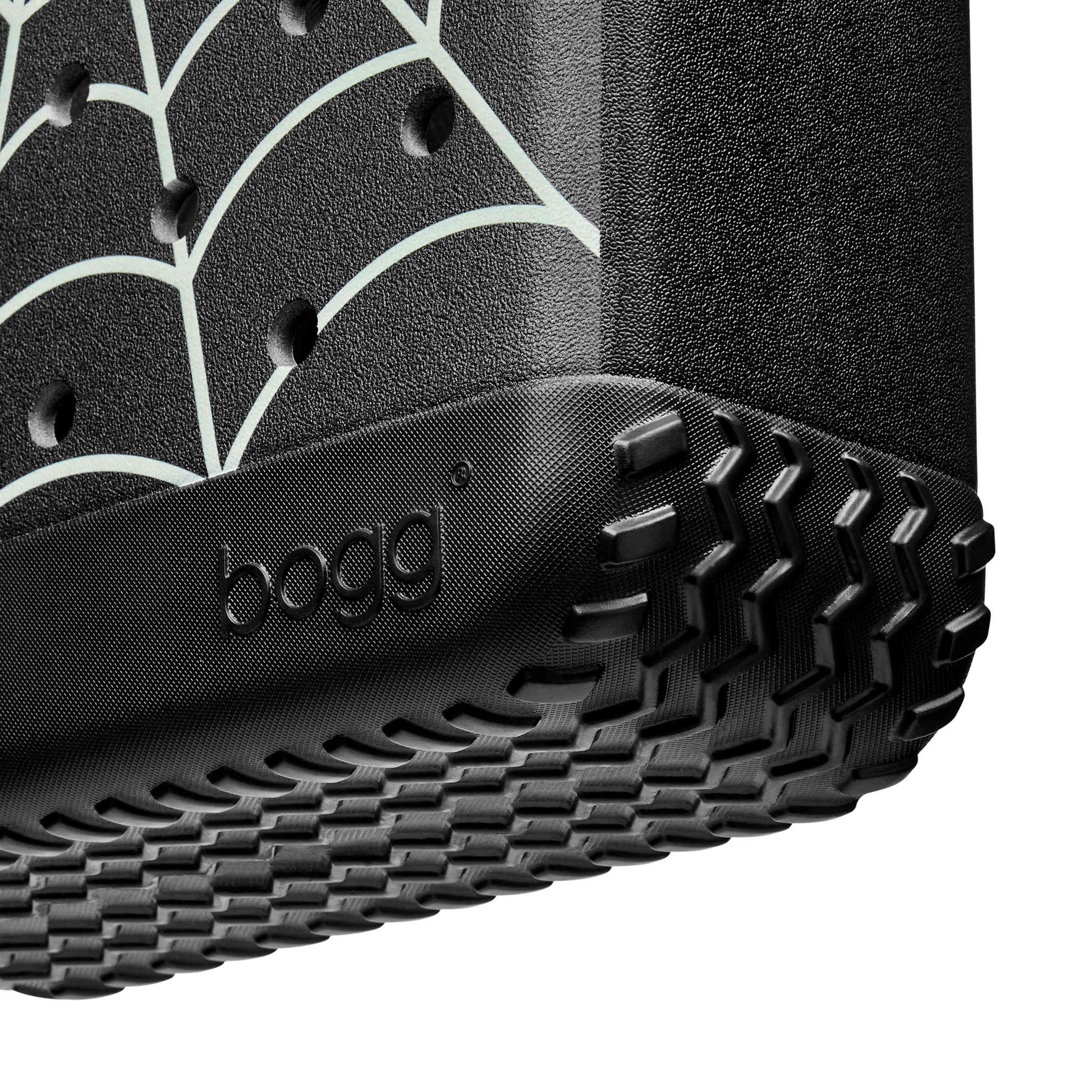 Close-up of a black Bogg Bag with a rugged treaded bottom edge and a white spiderweb pattern on the side, shown against a white background.