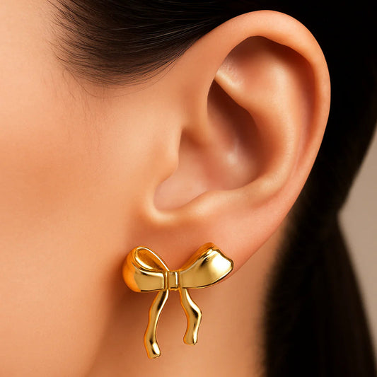Gold bow-shaped earring on a person's ear with a neutral background