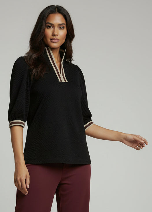 Woman wearing a black top with striped trim and burgundy pants on a gray background