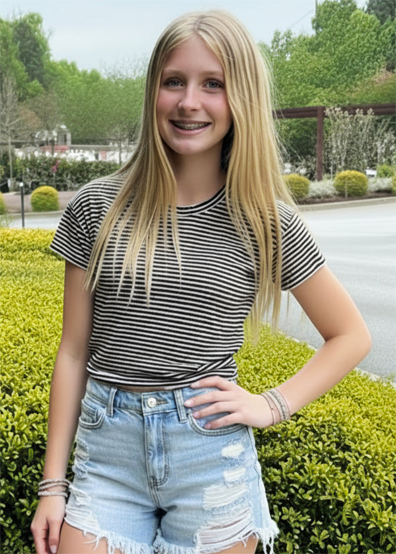 Young woman wearing a striped shirt and denim shorts standing outdoors.
