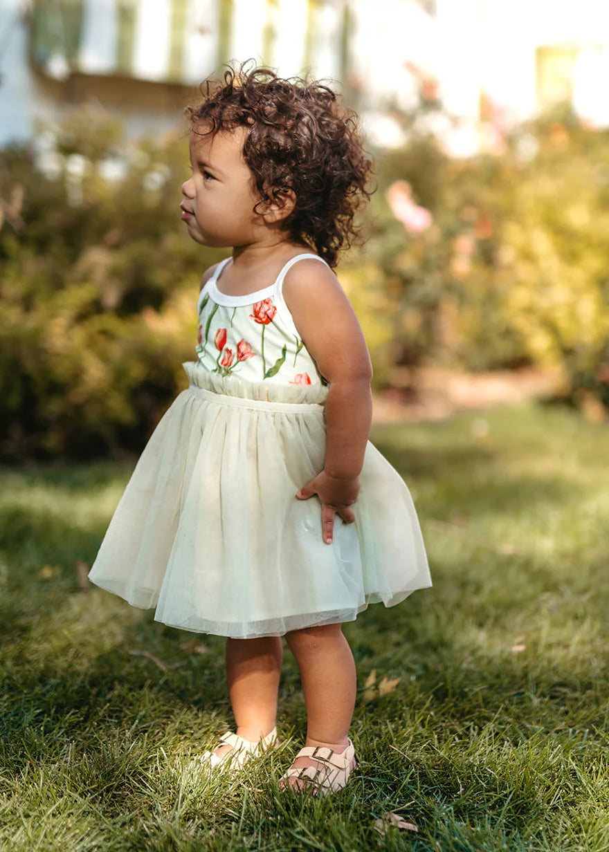Child in a floral dress standing on grass with a blurred background
