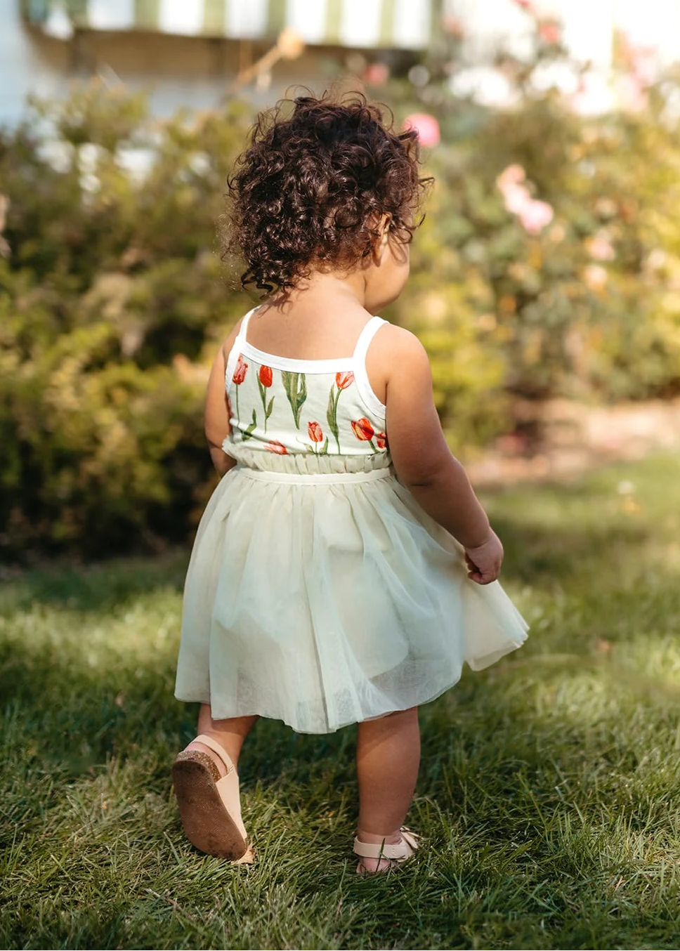 Child in a floral dress standing on grass with a blurred background