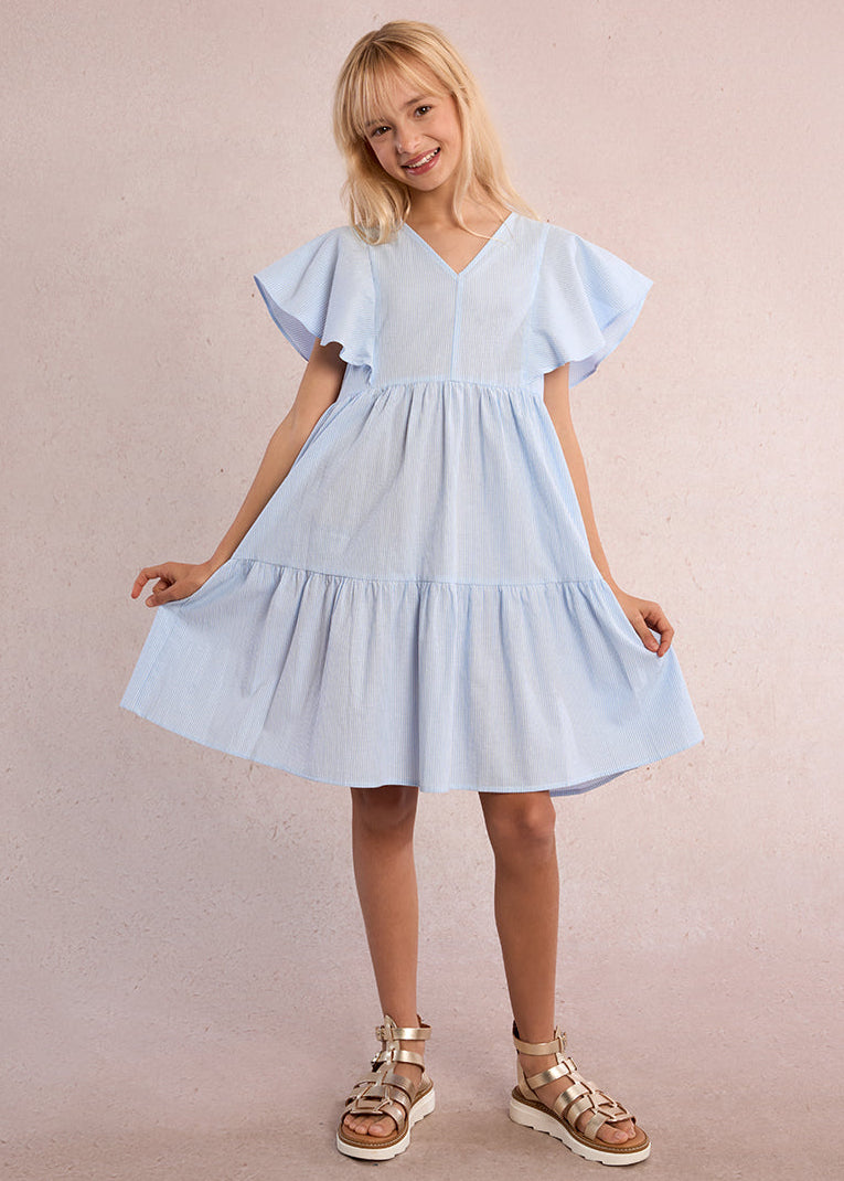 Young girl wearing a light blue dress with ruffled sleeves against a beige background