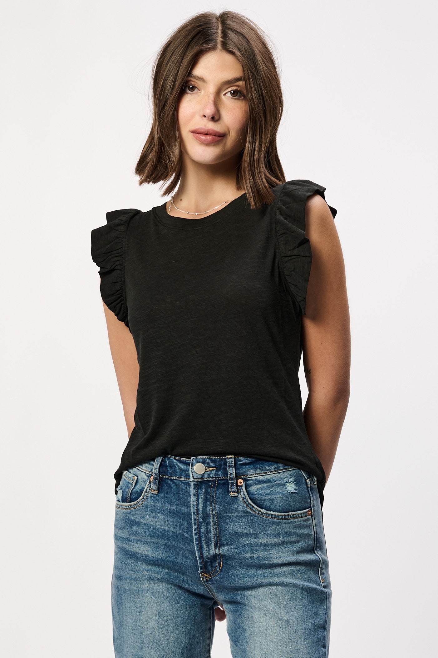 Woman wearing a black sleeveless top with ruffled shoulders and blue jeans on a white background