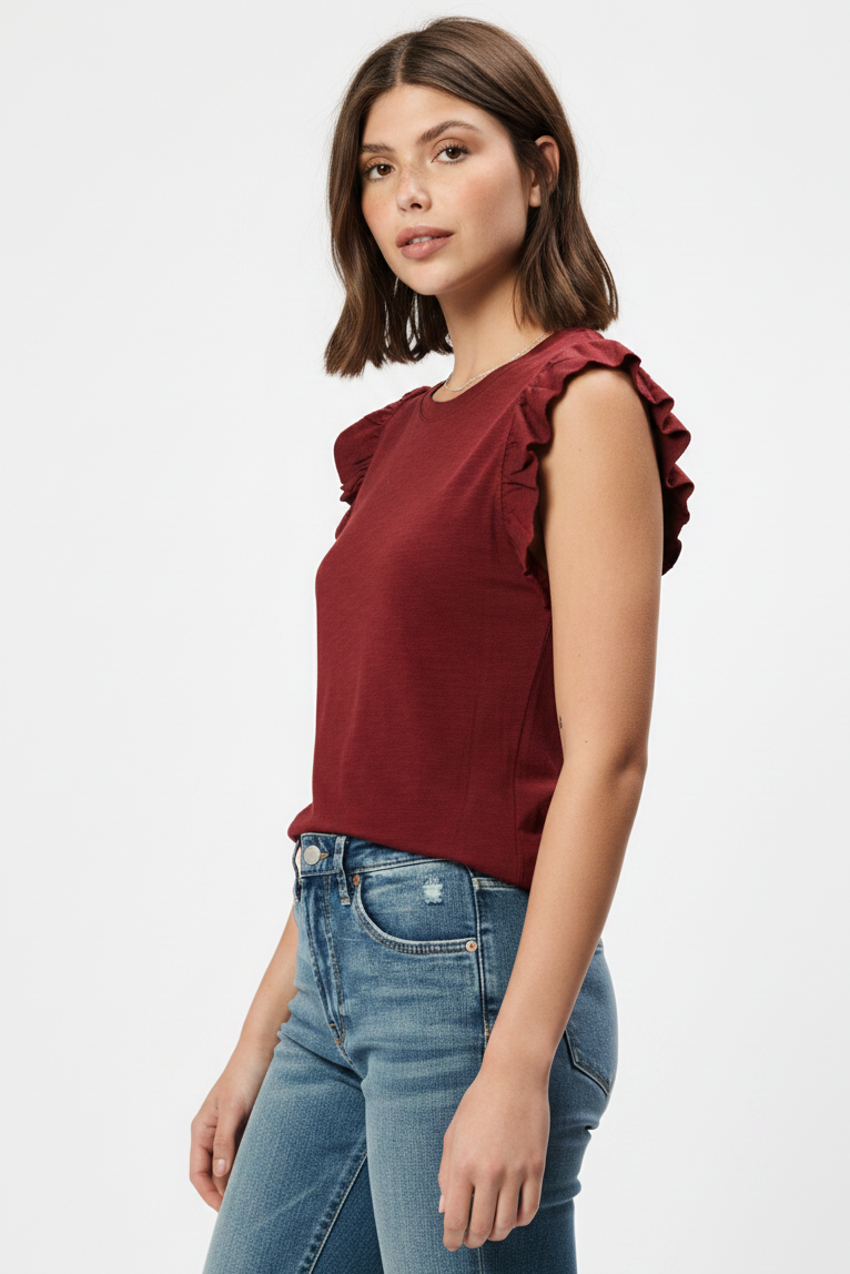 A woman wearing a sleeveless crewneck top in a deep burgundy red, featuring ruffled detailing on the shoulders, paired with blue jeans against a plain white background.
