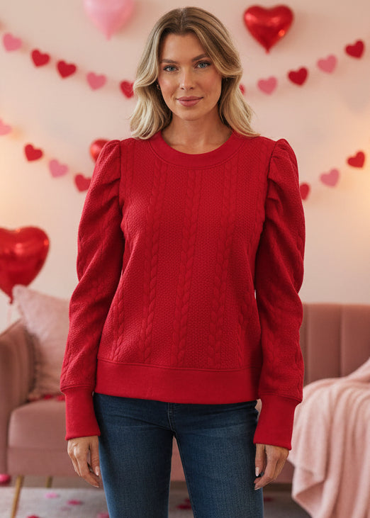 Woman wearing a red sweater in a cozy living room with a fireplace and Christmas stockings.