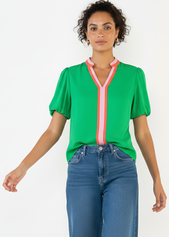 Woman wearing a green blouse with pink accents and blue jeans on a white background