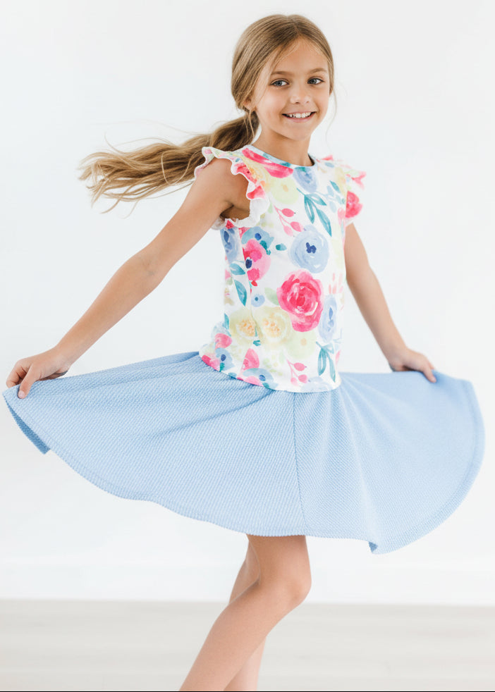 Child wearing a colorful floral top and light blue skirt on a white background